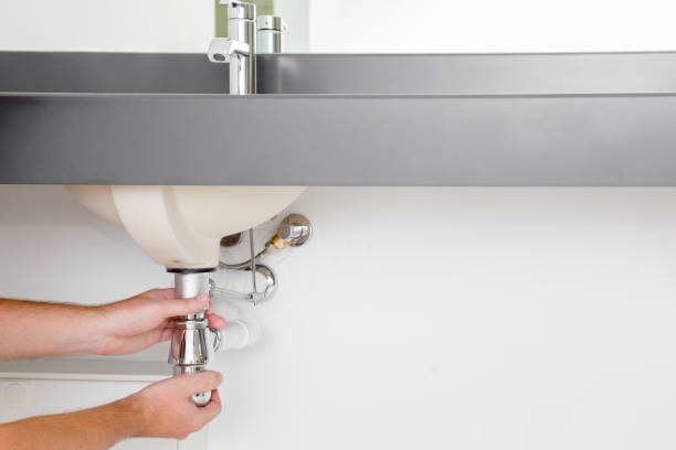 Man's hand checking new metal siphon under the sink.